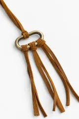 Collar largo de diseño artesanal con cordón de cuero tostado regulable, pieza metálica ovalada en tono bronce y flecos de cuero colgantes.