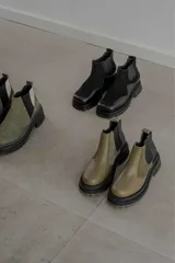 Botas tipo Chelsea con diseño bicolor en tonos negro y verde oliva. Presentan paneles laterales elásticos, suela track robusta y tirador trasero.