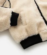 Campera de fleece color beige con diseño de paneles, costuras expuestas en color negro y cierre frontal. Posee cuello alto, mangas largas con puños elásticos y forro interior.