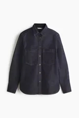 Camisa de denim de algodón rígido en color azul oscuro, con cuello clásico, cierre frontal de botones, bolsillos de parche en el pecho, mangas largas con puños abotonados y bajo redondeado.