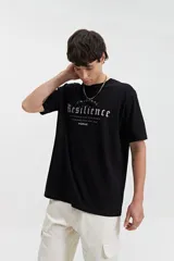 Remera de manga corta color beige, con escote redondo y fit regular. Presenta un estampado frontal en color marrón con la palabra "Resilience" en tipografía gótica y el texto "Original The World Has Changed Established Since 1976 // NLD Mistral".