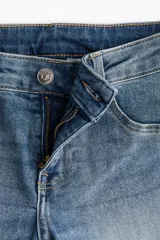 Pantalón jean acampanado de tiro bajo en denim levemente elástico, con bolsillos delanteros decorativos, bolsillo monedero y bolsillos abiertos atrás.