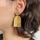 Aros colgantes con base superior negra y pieza inferior transparente con diseño de ojo grabado.