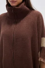 Poncho de tejido grueso, color negro y gris, con diseño de franjas diagonales y cuello alto con cierre. Presenta terminaciones con flecos.