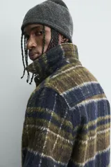Sobrecamisa de corte relajado confeccionada en tejido con textura efecto pelo. Presenta diseño de cuadros en tonos verde y negro, cuello solapa, cierre frontal con botones, manga larga con puños abotonados y un bolsillo de plastrón en el pecho.