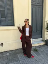 Conjunto de dos piezas compuesto por un blazer y un pantalón de corte sastrero, confeccionados en tela de algodón con estampado de rayas verticales blancas sobre fondo gris. El blazer presenta solapas clásicas y cierre frontal, mientras que el pantalón es de tiro medio y pierna recta.