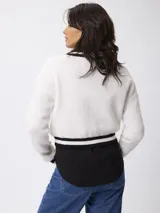 Sweater de punto estilo preppy, color blanco con detalles de rayas negras en el escote en V, puños y ruedo. De corte holgado y manga larga.