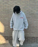 Hoodie de corte regular en color gris melange, con capucha, mangas largas y bolsillos tipo canguro. Presenta un estampado gráfico en la espalda con la inscripción 'Fletes' y una ilustración de una grúa transportando una planta.