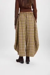 Pantalón de corte holgado con silueta tipo balloon, confeccionado en tela a cuadros. Presenta cintura elástica con cordón ajustable y cortes laterales circulares que aportan volumen a la prenda.