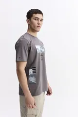 Remera de manga corta color gris oscuro con cuello redondo y un estampado rectangular frontal que simula una obra de arte paisajística en blanco y negro.