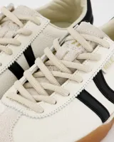 Championes deportivos de estilo retro color blanco con detalles en negro, suela fina color caramelo, capellada de cuero y nylon, lengüeta semitransparente acolchada, cordones bicolor intercambiables y cuello acolchado.