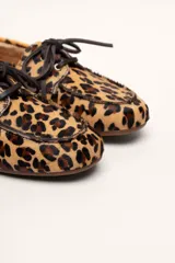 Mocasín tipo boat shoe color marrón, confeccionado en cuero, con cordones de cuero marrón y cordones decorativos azules.