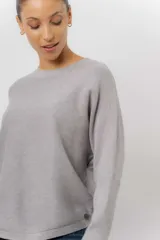 Buzo tejido de punto en color beige, con cuello redondo, mangas largas y silueta relajada con dobladillo irregular, siendo más largo en la parte trasera.