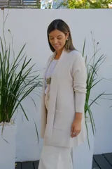 Saco abierto tipo cárdigan color crudo, de corte recto y largo medio, con mangas largas y dos bolsillos frontales aplicados.