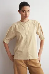 Camisa de manga corta color beige con sutiles rayas verticales blancas, cuello mao y cierre frontal oculto con botones.