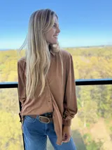 Camisa de manga larga confeccionada en tela simil gamuza, color marrón tostado, con cuello clásico y cierre frontal de botones.