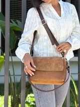 Cartera bandolera de cuero gamuzado color camel, con solapa frontal y cierre principal. Incluye dos correas desmontables, una corta y una larga regulable, y cuenta con bolsillo interior.