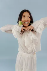 Camisa de estilo romántico confeccionada en algodón, con cuello alto, volados frontales y mangas largas con puños acampanados también decorados con volados.