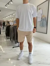 Bermuda de jogging color beige, con bolsillos laterales y estampa con texto blanco en la pierna izquierda.
