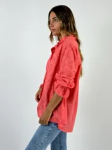 Camisa de algodón con diseño de broderie, color coral, con cuello camisero, cierre frontal de botones y mangas largas con volados en los puños.