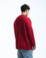 Sweater unisex de lana merino fina color rojo, con cuello redondo y corte relajado. Presenta un motivo inspirado en la técnica de zurcido visible.