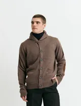 Cardigan de punto color marrón con cuello esmoquin, cierre frontal con botones y presilla superior. Presenta mangas largas con coderas en contraste y bolsillos frontales de ribete.