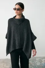 Capita de tejido de punto grueso en color gris oscuro, con cuello alto y diseño holgado tipo poncho.