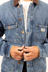 Campera de jean azul con cuello de corderito marrón, cierre con botones metálicos, cuatro bolsillos frontales y puños con botón.