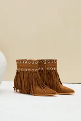 Bota texana de gamuza color camel, con taco cuadrado y punta fina. Cuenta con flecos largos colgantes y detalles de ojalillos metálicos plateados en la parte superior.