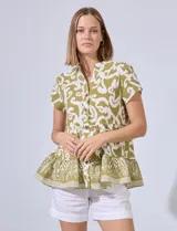 Blusa verde con estampado de arabescos blancos, cuello mao, escote en V y abertura central con botones. Corte en la cintura con frunces y terminación en ruedo con volados.