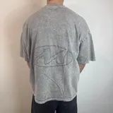 Remera de corte boxy fit con efecto lavado tipo snow wash, color gris. Presenta un diseño lineal bordado en la espalda con forma ovalada.