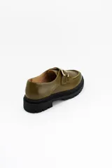 Mocasines de cuero color verde oliva con suela track negra de plataforma. Presentan una tira decorativa sobre el empeine con hebilla metálica dorada ajustable en el lateral.