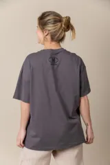 Remera gris con estampa de la letra M en negro y cadena plateada en el cuello.