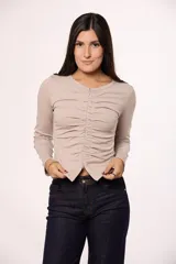Remera de manga larga color beige, confeccionada en algodón, con diseño ajustado al cuerpo. Presenta un frunce central vertical con cierre frontal que permite regular la apertura en la parte inferior.