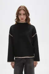 Polera de tejido de punto color negro con detalles de vivos en color beige en el cuello, puños, ruedo y costuras de las mangas. Presenta un diseño holgado con cuello alto y mangas largas.