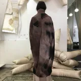 Poncho de lana merino afieltrada color marrón con cuello alto y abertura frontal.