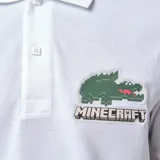 Chomba blanca de piqué de algodón con cuello clásico y tapeta de dos botones. Presenta logo de Lacoste y cocodrilo pixelado de Minecraft bordados en el pecho.