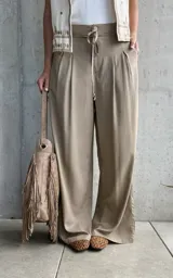 Pantalón palazo de lino color tostado, de calce amplio y fluido, con tablas en el frente y cordón ajustable en la cintura.