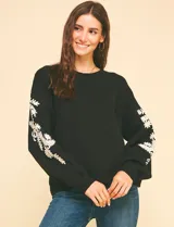 Suéter de punto negro con cuello redondo y bordados florales en hilo dorado en ambas mangas.