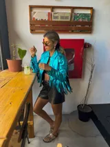Campera turquesa de tela brillante con flecos en mangas y ruedo.