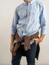 Camisa de corte regular confeccionada en tejido Oxford de algodón, con diseño de rayas verticales finas. Presenta cuello abotonado, cierre frontal con botones y un bolsillo en el pecho.
