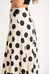 Falda midi color crudo con estampado de lunares negros, corte evasé y cintura alta.