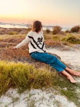 Sweater de lana color crema con cuello redondo, mangas largas y diseño con apliques de cuero negro en forma de V en el frente y bordado de una rosa negra en el pecho.