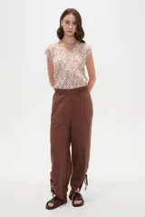 Pantalón ancho color marrón, de tiro alto con cintura elástica y detalles de frunces con tiras ajustables en los tobillos.