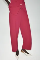 Pantalón de tiro bajo color fucsia, con pliegues delanteros, bolsillos frontales, pernera holgada y cierre frontal con cremallera y botón.