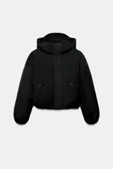 Chaqueta acolchada de corte corto con cuello subido y capucha. Presenta cierre frontal con cremallera termosellada y solapa con botones a presión, bolsillos laterales con cierre, mangas largas con puños elásticos y bajo ajustable con cordones.