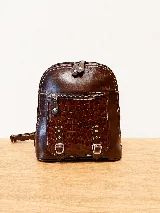 Mochila de cuero vacuno color marrón, con diseño estructurado y combinación de textura croco en el bolsillo frontal. Cuenta con un compartimento principal con cierre, un bolsillo frontal con cierre metálico y hebillas decorativas, y correas regulables.