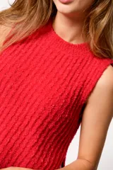 Chaleco de punto texturizado color rojo, con cuello redondo y diseño sin mangas. Presenta un corte recto con aberturas laterales y un largo asimétrico, siendo más corto en la parte frontal.