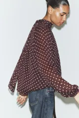 Blusa de cuello subido con diseño de lunares, manga larga abullonada con puños elásticos y forro interior.