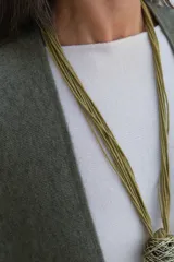 Collar largo de estilo artesanal con cordones de hilo color verde oliva, que presenta un dije central esférico compuesto por hilos metálicos entrelazados y una borla colgante del mismo tono.